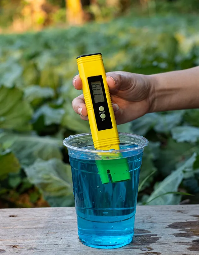 A yellow digital pH meter in a cup of blue liquid.