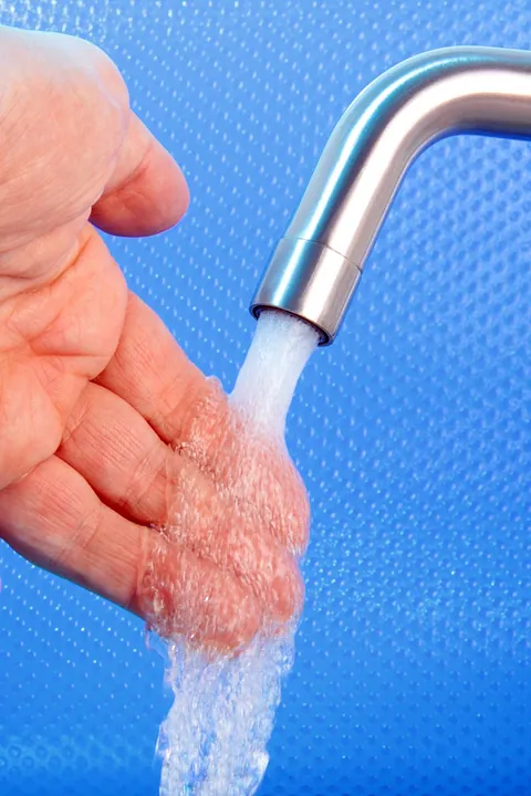 A hand placed under a stream of water against a blue background.